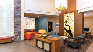 A modern hotel lobby with a stone accent wall, a seating area with sofas and armchairs, a wooden reception desk, and a large wall art piece. - Hyatt Place Canton (North Canton)