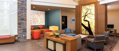 A modern hotel lobby with a stone accent wall, a seating area with sofas and armchairs, a wooden reception desk, and a large wall art piece.