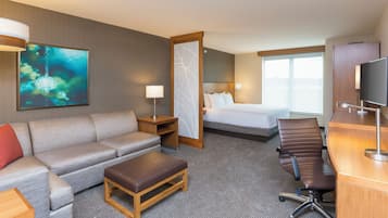 Ein Hotelzimmer mit einer Couch, einem kleinen Holztisch, einem Schreibtisch mit Stuhl, einem Bett, einem Fernseher und einem großen Fenster.
