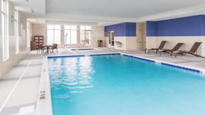 A large indoor pool with clear blue water, surrounded by lounge chairs and a small seating area with a table and chairs. - Hyatt Place Canton (North Canton)