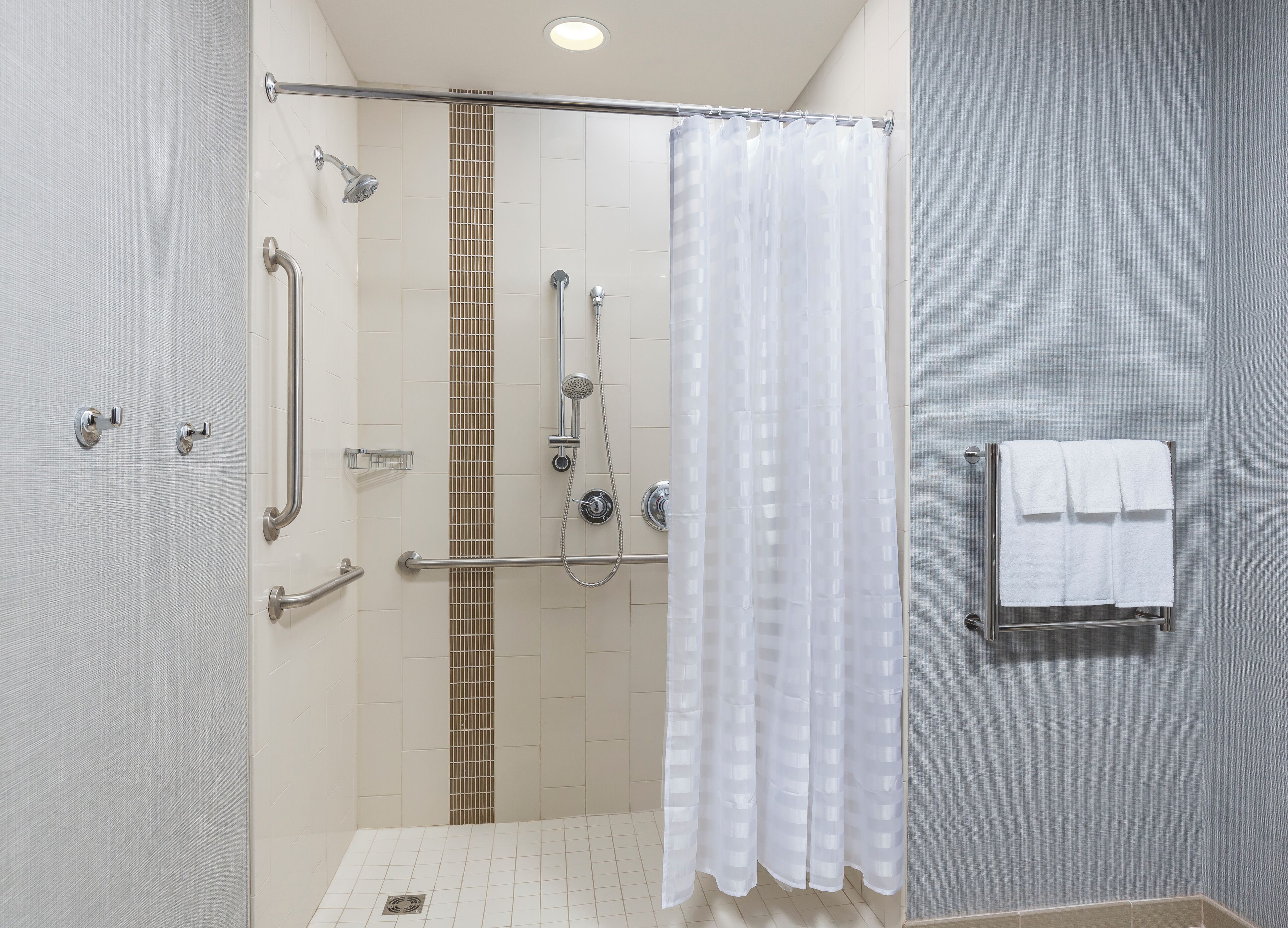 A modern shower area with a glass partition, grab bars, and a towel rack.