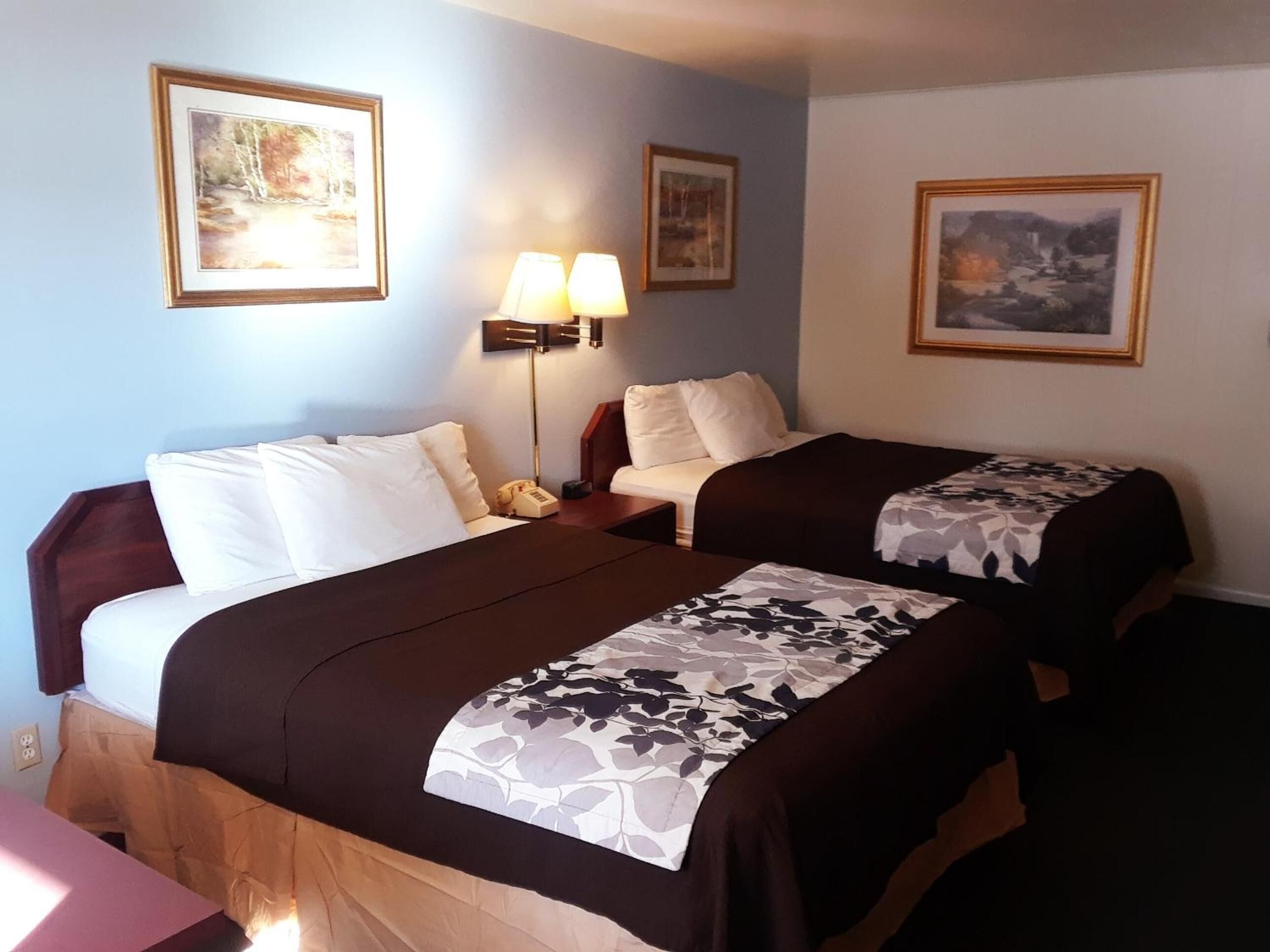 A hotel room with two beds, a desk, and a lamp.