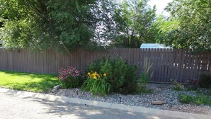 A garden with a wooden fence, gravel path, and flowering plants. - Budget Inn Express (Sheridan)