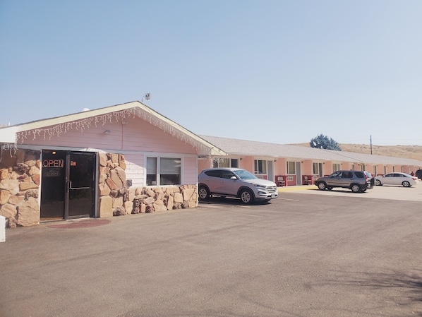Un motel con fachada de piedra, un letrero que dice 'OPEN' y un área de estacionamiento con varios autos.