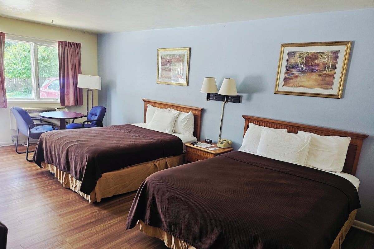 A hotel room with two beds, a desk with a chair, a lamp, and framed pictures on the wall.