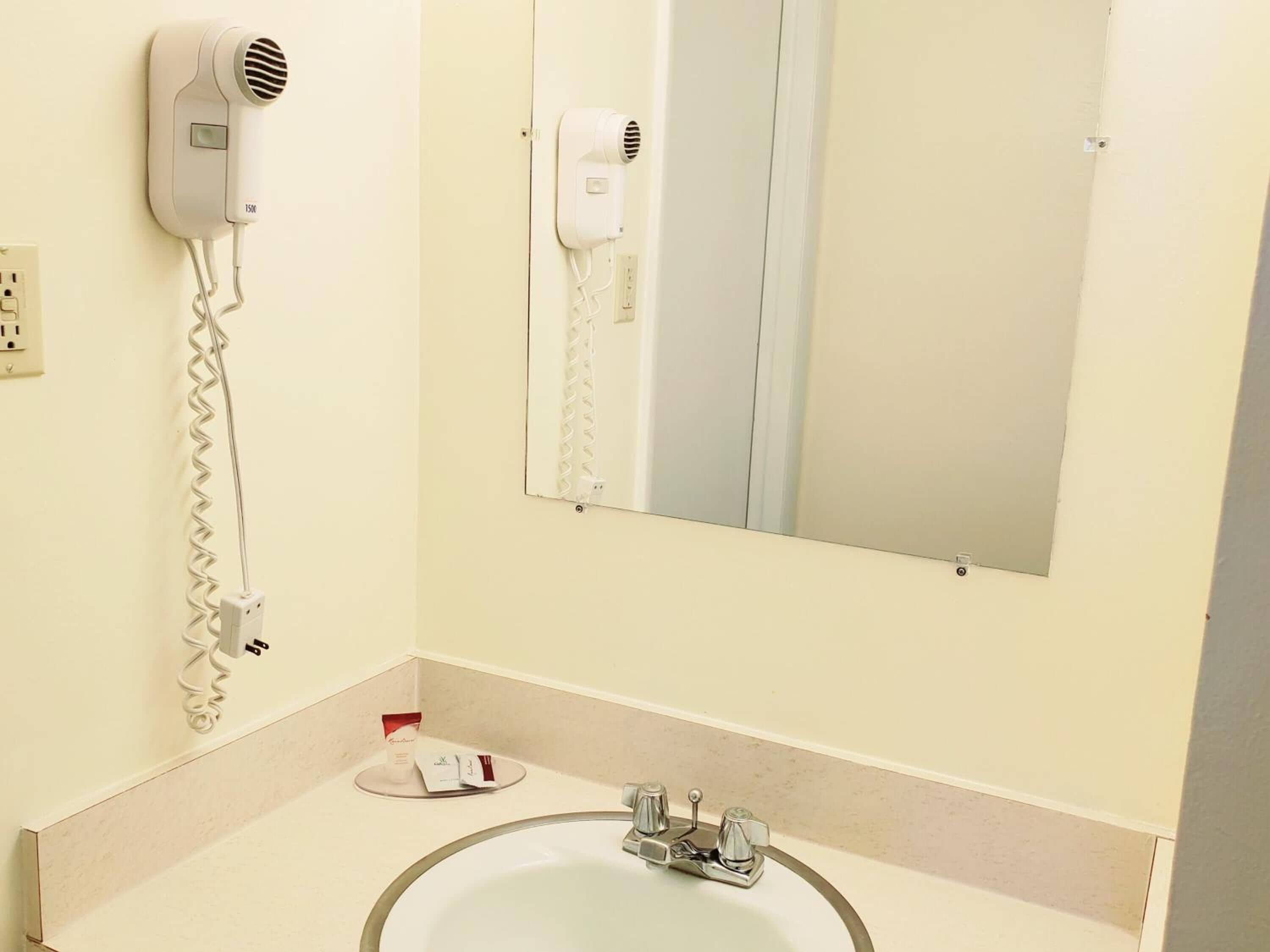 Un baño con un lavamanos, dos secadores de pelo fijos en la pared y artículos de aseo sobre el mostrador.