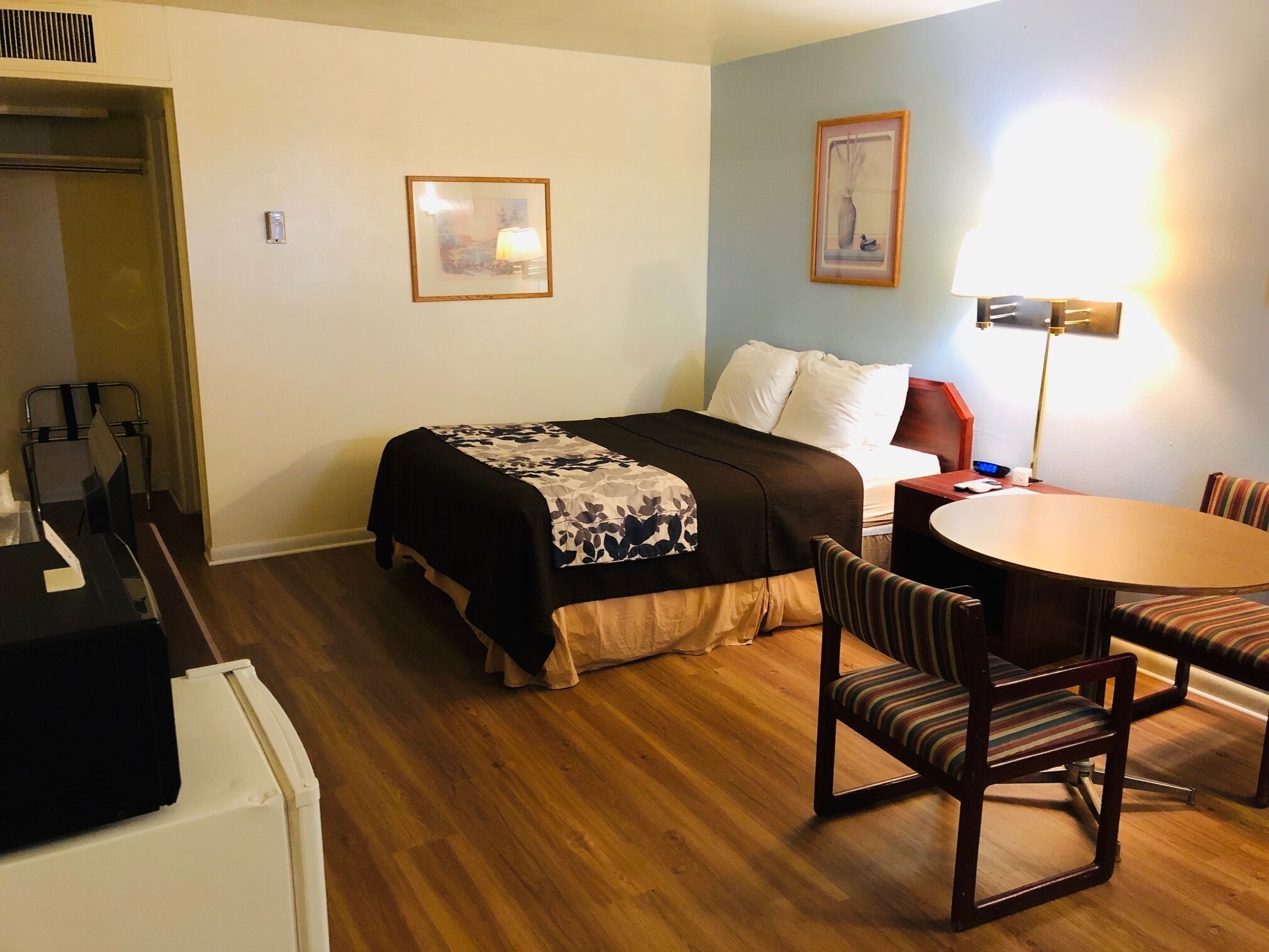 A hotel room with a bed, a desk, a chair, a table, and a lamp.