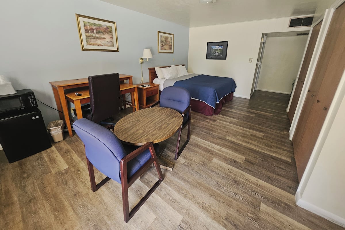 A room with a bed, a desk, a chair, a small table, and a microwave.