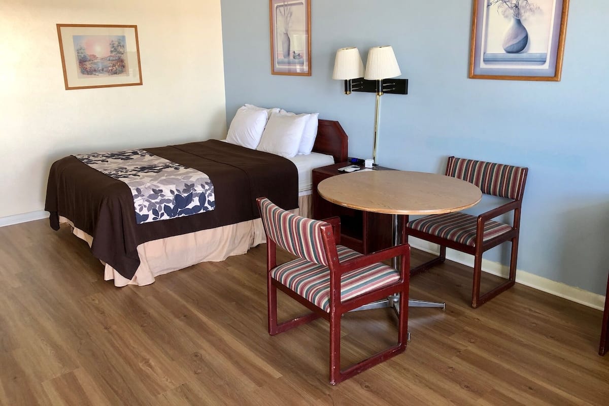 A hotel room with a bed, a bedside table, a lamp, a round table with two chairs, and framed artwork on the walls.