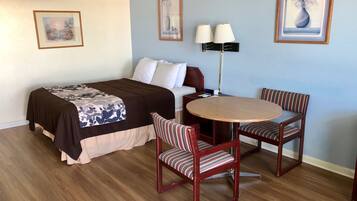 A hotel room with a bed, a bedside table, a lamp, a round table with two chairs, and framed artwork on the walls.