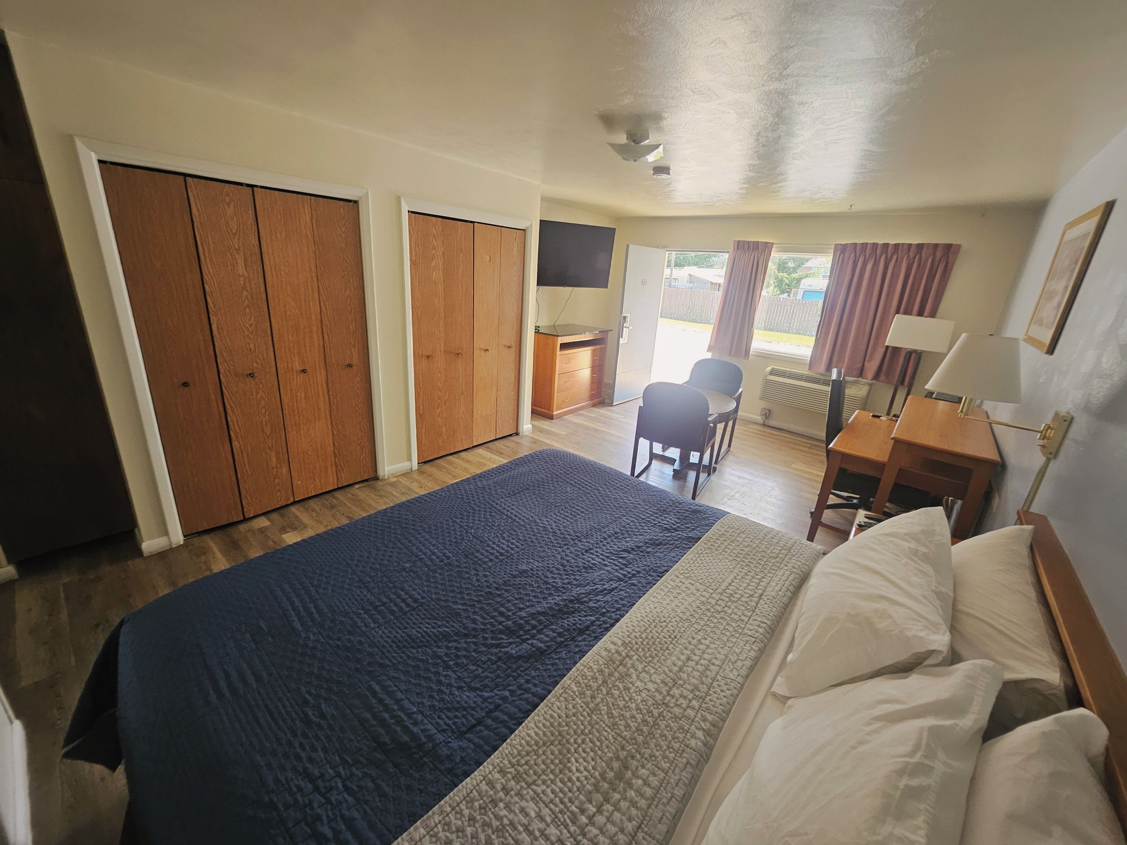 A hotel room with a bed, a desk, a chair, and a view of the outside.
