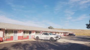 Um motel com uma fileira de quartos, estacionamento e céu claro.