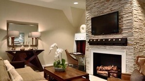 A living room with a stone fireplace, a television mounted above it, and a dining area with a table and chairs. - Graylyn Estate (Winston-Salem)