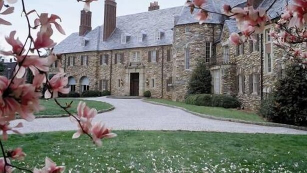 A stone building with a central entrance, surrounded by a well-maintained lawn and a pathway leading to the entrance. - Graylyn Estate (Winston-Salem)