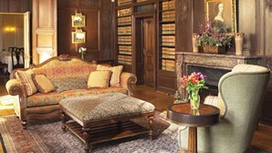 A library with a large, ornate sofa, a small round table with a vase of flowers, and a fireplace with a portrait above it. - Graylyn Estate (Winston-Salem)