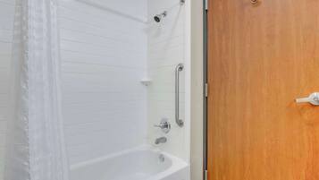 A bathroom with a white bathtub, a shower, and a wooden door.