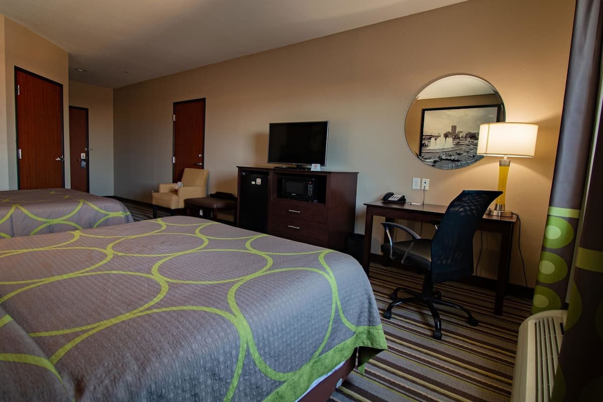 A hotel room with two beds, a desk with a chair, a television, and a mirror.