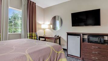 A hotel room with a bed, a desk with a lamp, a television, a microwave, and a refrigerator.