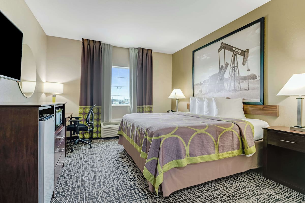 A hotel room with a bed, desk, chair, and a large painting on the wall.