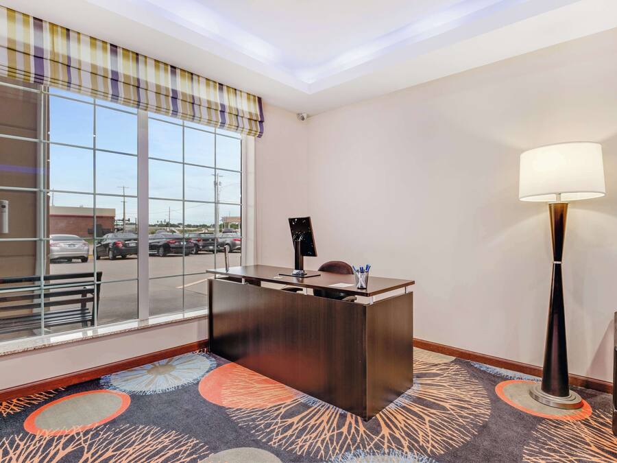 Zona de recepción de un hotel con un mostrador, un ventanal grande, una lámpara y suelo alfombrado.