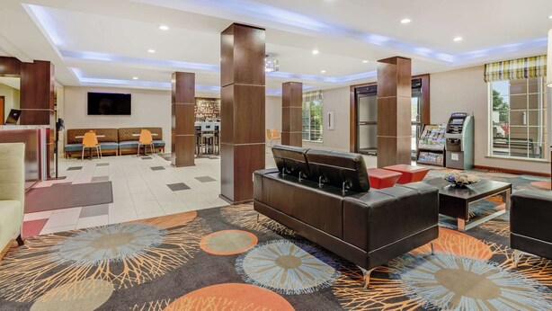 Un vestíbulo de hotel con zona de estar, mostrador de recepción y quiosco de autoservicio.