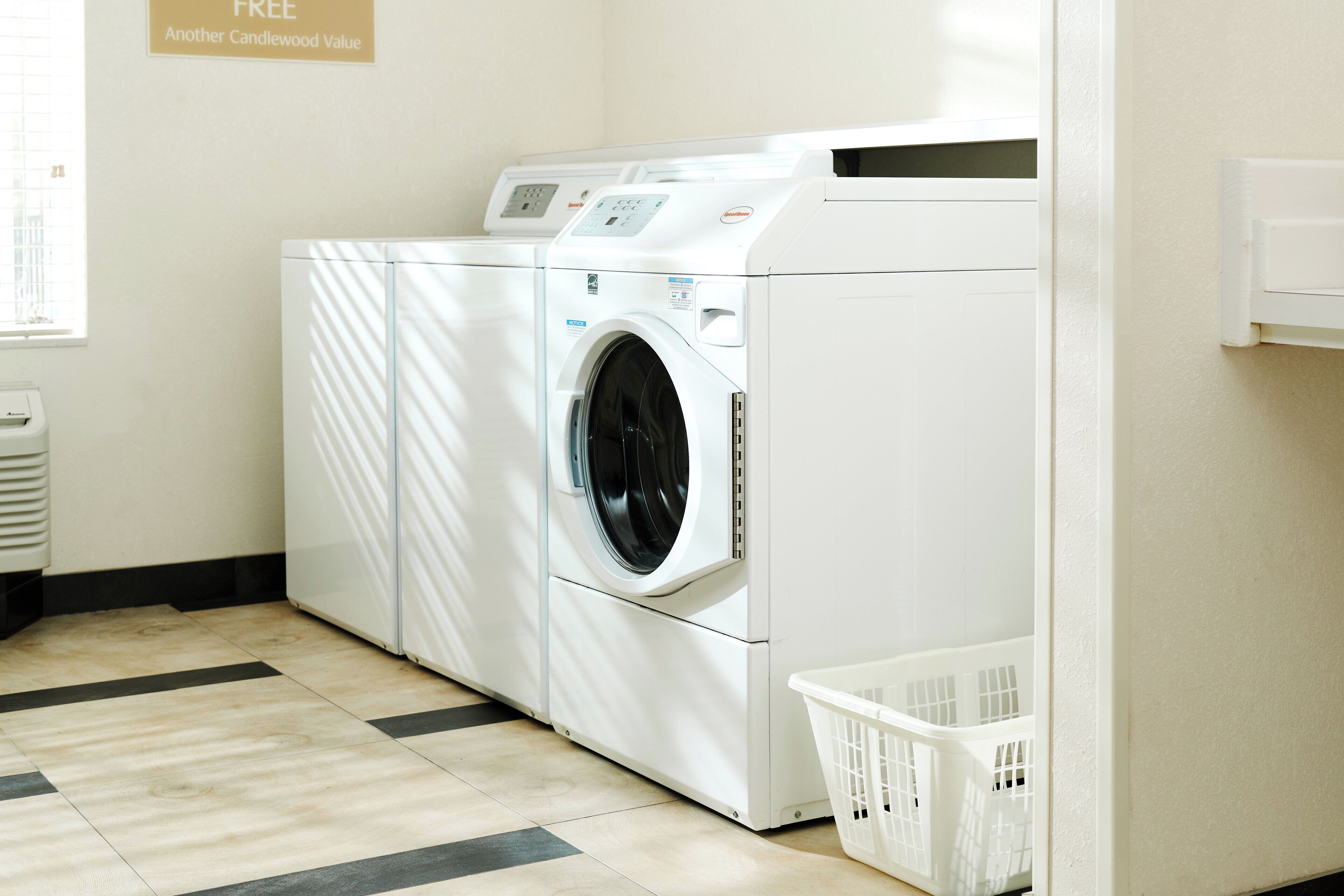 A laundry room with a front-loading washer and dryer, a white basket, and a tiled floor.