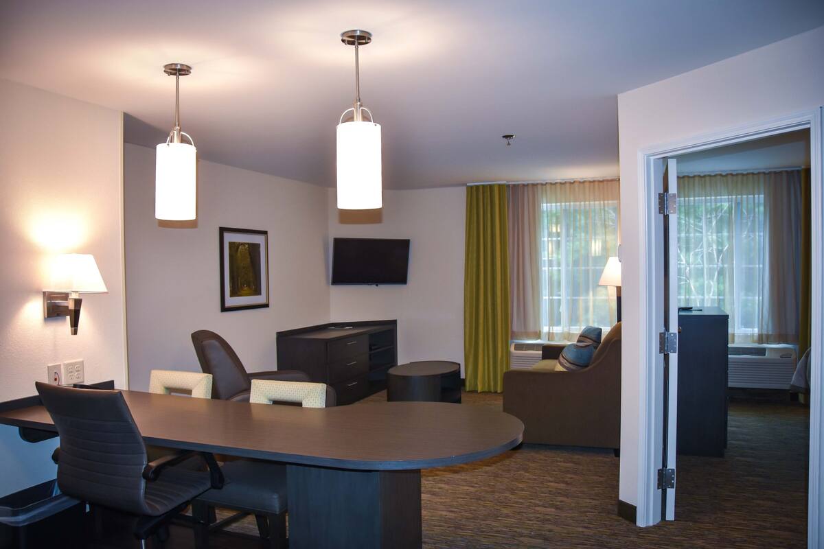 Une chambre d’hôtel équipée d’une table de conférence, de deux chaises, d’un canapé, d’une télévision et d’une fenêtre avec des rideaux.