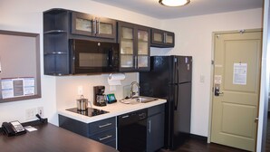 A compact kitchen with dark cabinetry, a built-in microwave, a refrigerator, and a dishwasher. - Candlewood Suites Columbus-Northeast by IHG (Columbus)