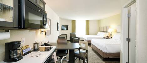 A hotel room with a kitchenette, a bed, a desk, and a chair.