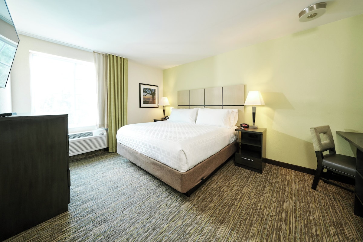Een hotelkamer met een groot bed, twee nachtkastjes met lampen, een bureau, een stoel en een raam met gordijnen.