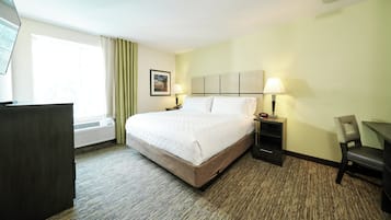 Una habitació d'hotel amb un llit gran, dues taules de nit amb làmpades, un escriptori, una cadira i una finestra amb cortines.