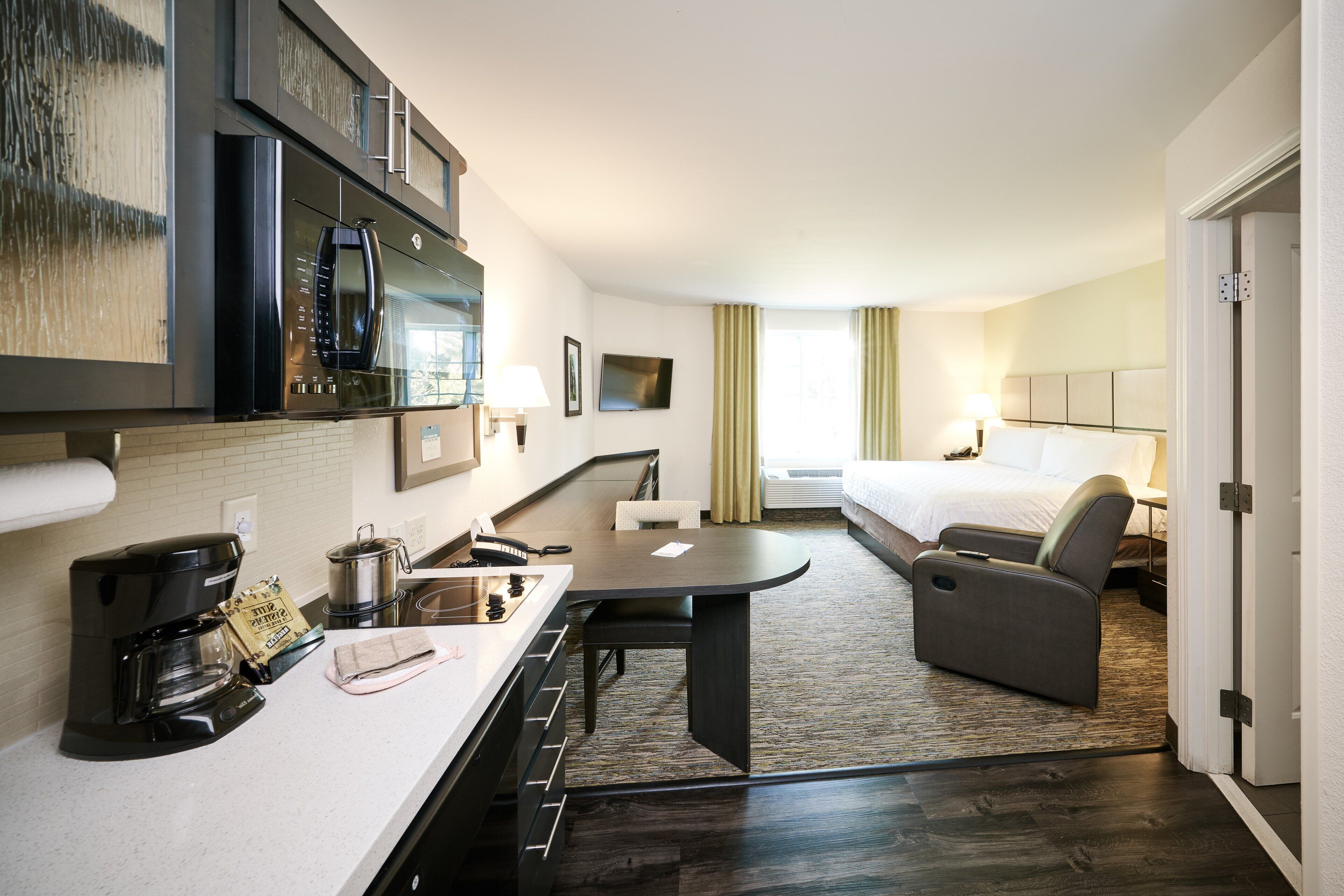 A hotel room with a kitchenette, a bed, a seating area, and a TV.