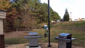 Two barbecue grills in an outdoor setting with a paved walkway, trees, and a grassy area. - Candlewood Suites Columbus-Northeast by IHG (Columbus)