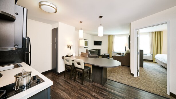 A modern hotel room with a kitchen area, a dining table, and a seating area with a sofa and chairs. - Candlewood Suites Columbus-Northeast by IHG (Columbus)
