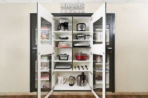 A kitchen cabinet with various appliances and items, including a coffee maker, a slow cooker, and a toaster.