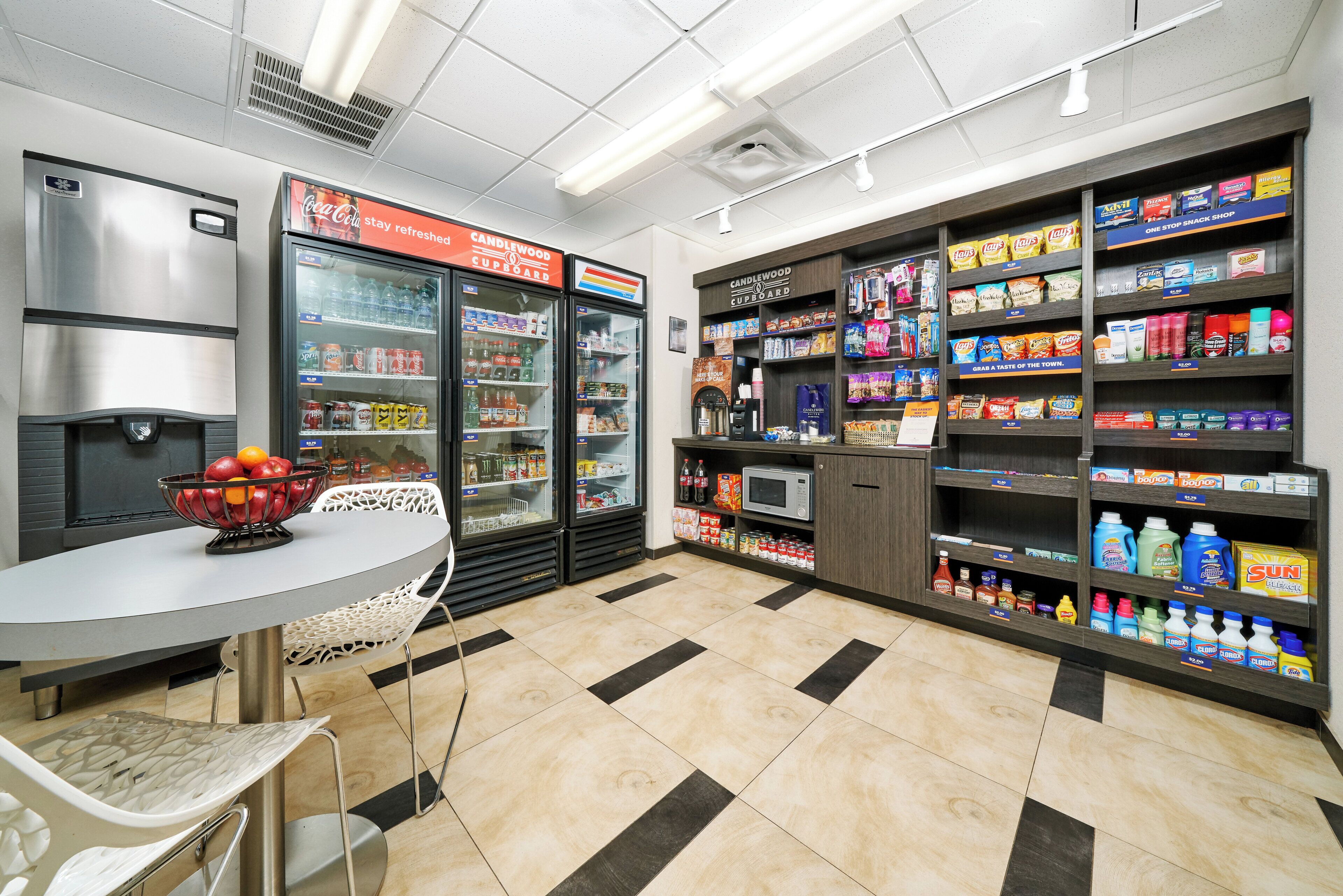 A clean, well-lit convenience store with refrigerated beverage dispensers, snack shelves, and a microwave.