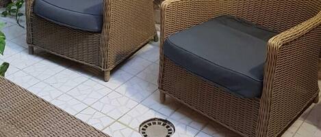 Un conjunto de sofá y sillón de mimbre frente a una pared de piedra, con una pequeña maceta blanca y una planta de hiedra.