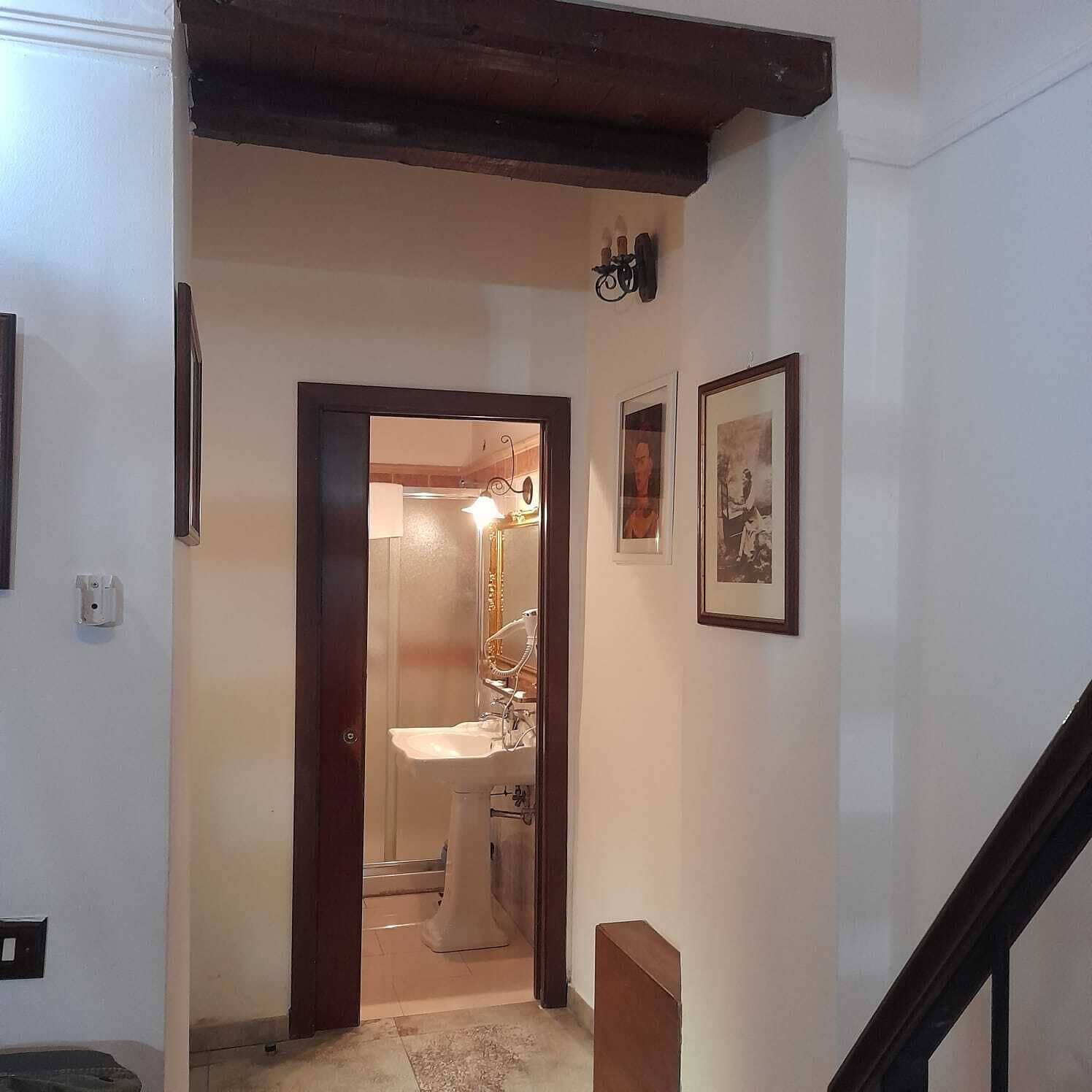 A hallway with a wooden staircase, a door leading to a bathroom, and two framed pictures on the wall.