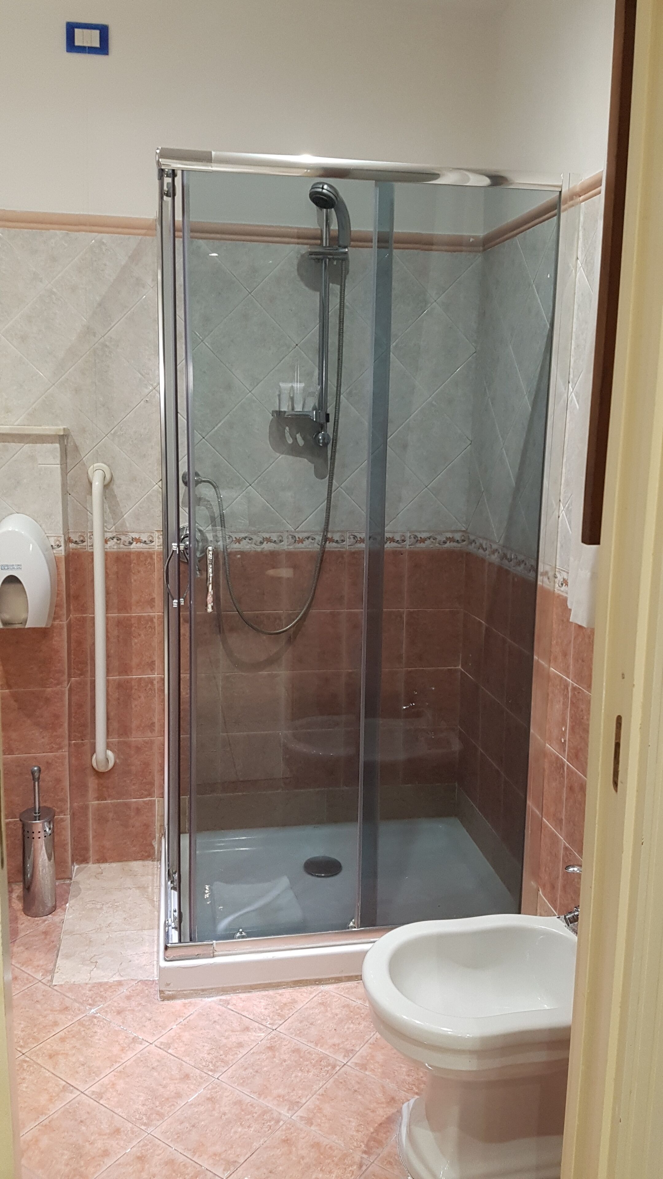 A glass-enclosed shower with a handheld showerhead and a wall-mounted faucet.