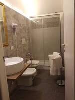 Un bagno moderno con un lavandino rotondo, due servizi igienici, una cabina doccia in vetro e un porta asciugamani.