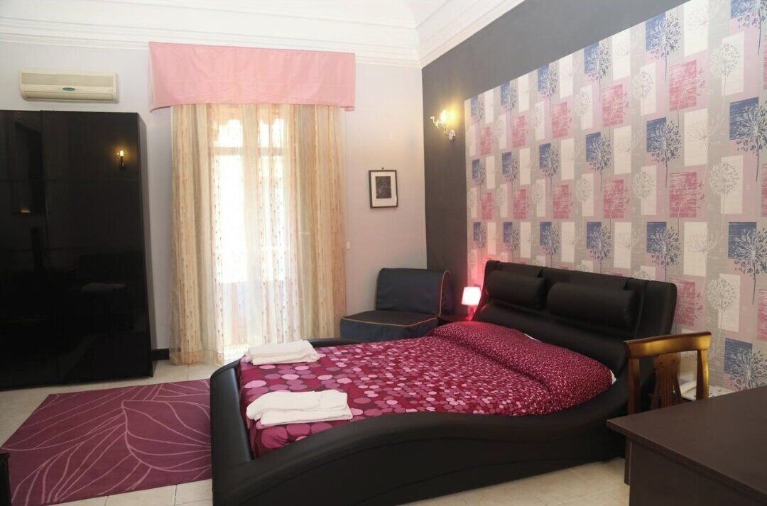 A bedroom with a bed, a desk, a chair, a wardrobe, and a window with curtains.