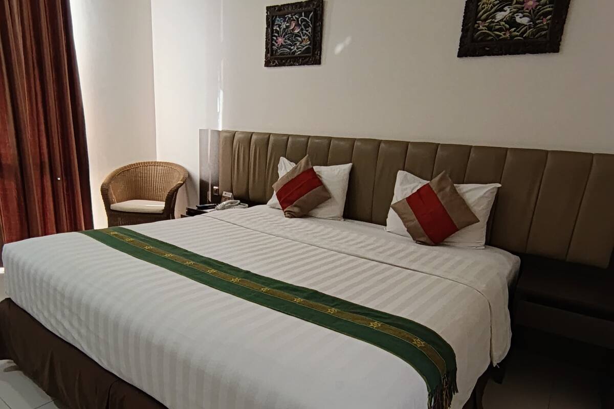 A hotel room with a large bed, a chair, two wall-mounted artworks, and a curtain.