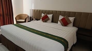 A hotel room with a large bed, a chair, two wall-mounted artworks, and a curtain.