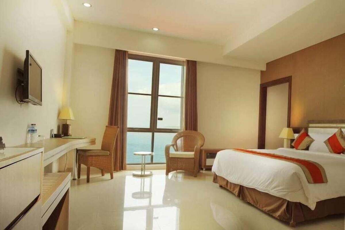 A hotel room with a bed, a desk, a chair, a small table, and a TV.