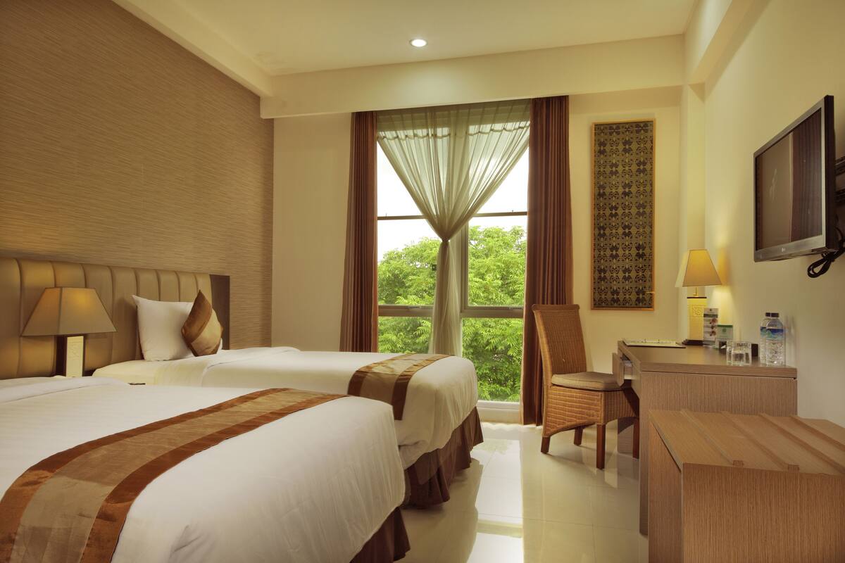 A hotel room with two beds, a desk, a chair, a television, and a window with curtains.