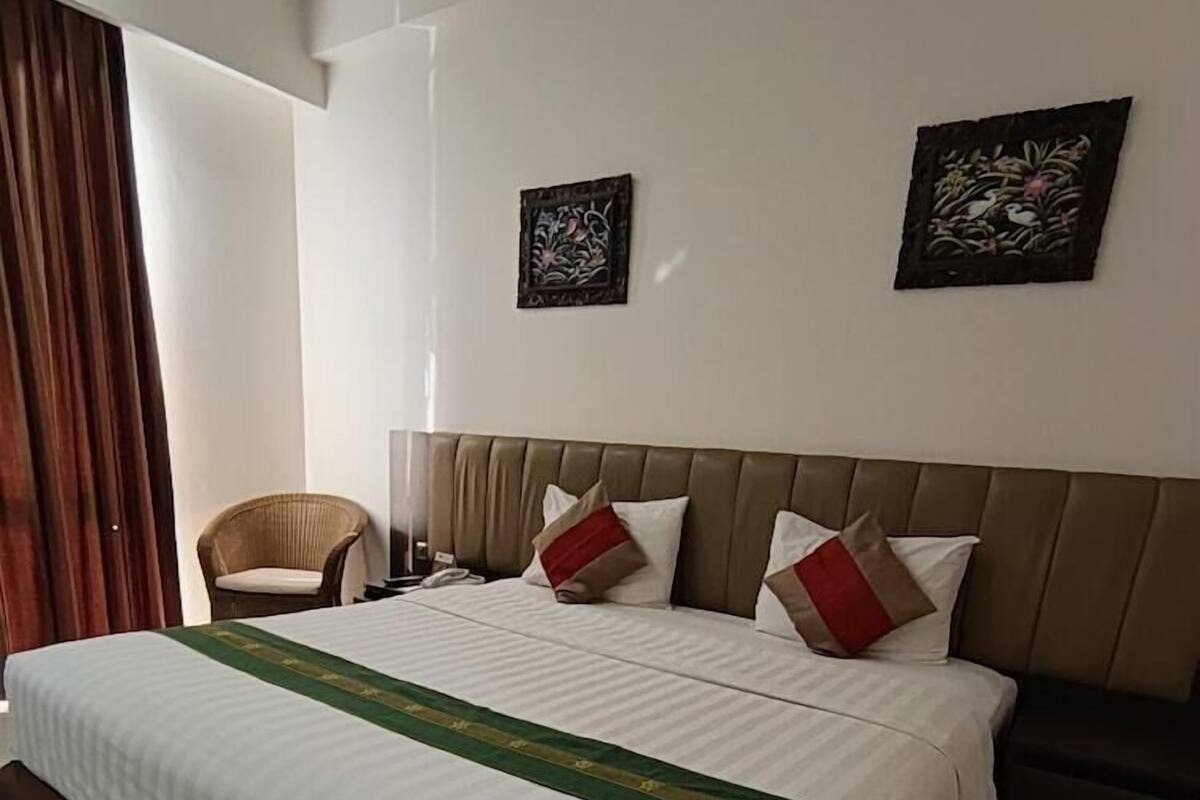 A hotel room with a large bed, a chair, two wall-mounted artworks, and a curtain.