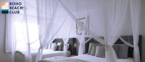 Habitación de hotel con dos camas, cada una con dosel. El suelo es de baldosas y hay un cuadro en la pared.
