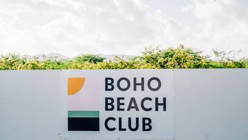A sign for Boho Beach Club with a partial view of greenery and mountains in the background.