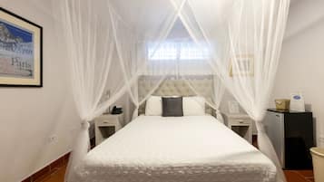 A neatly arranged bedroom with a bed under a white canopy, a nightstand, a small table, and a wall-mounted picture of Paris.