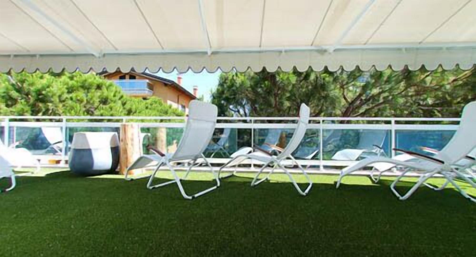 Un'area esterna coperta con poltrone da relax bianche e una piscina.